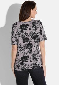 Korte mouwen top in lichtpaarse stof met zwart bloemenpatroon en ronde halslijn. Gladde textuur met een ontspannen pasvorm.