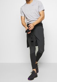 Camiseta atlética gris de manga corta, combinada con pantalones ajustados negros y zapatillas de running negras con detalles en púrpura.