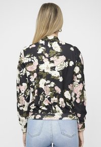 Top a maniche lunghe floreale caratterizzato da tessuto nero con fiori bianchi, rosa e verdi. Orlo e polsini arricciati, texture liscia.