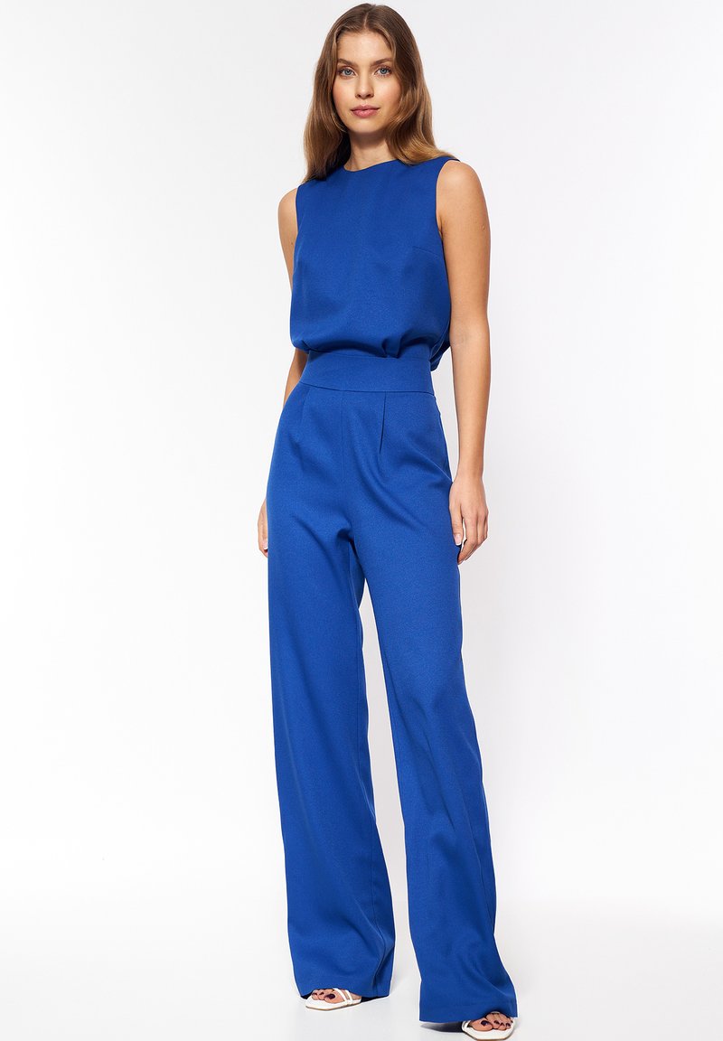 Niebieski kombinezon bez rękawów o wysokim stanie, szerokich nogawkach i gładkiej fakturze. Posiada prosty dekolt i subtelne drapowanie na górze.