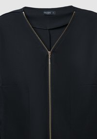 Schwarze Bluse mit V-Ausschnitt und einem goldenen Reißverschlussverschluss auf der Vorderseite. Hergestellt aus glattem Stoff mit zwei Seitentaschen. Größenetikett sichtbar.