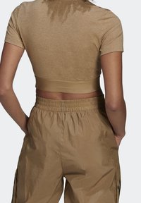 Brown cropped t-shirt made of smooth fabric, featuring a round neckline and fitted sleeves, paired with lightweight, elastic-waist cargo pants.
