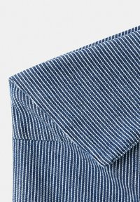 Tissu rayé verticalement bleu et blanc plié à un angle vif, montrant une texture détaillée et des coutures sur une surface plane.