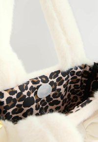 Geantă tip tote crem, pufoasă, cu mânere moi, căptușeală cu imprimeu leopard și detaliu de închidere magnetică. Are un exterior texturat și pufos.