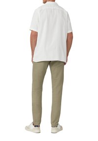 Chemise blanche à manches courtes, coupe décontractée, en tissu léger, assortie à un pantalon vert olive clair et des baskets blanches.