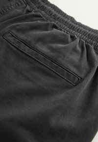 Pantaloni shorts neri con vita elasticizzata e una singola tasca posteriore caratterizzata da un design rettangolare e cuciture a contrasto. Tessuto testurizzato.