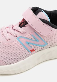 Baskets roses claires avec tige en mesh, col rembourré, accents bleus et une sangle en velcro. Présente une surface texturée et une semelle en caoutchouc blanc.