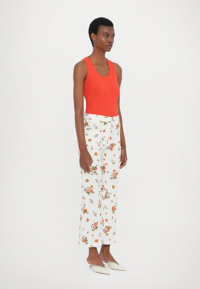 Red ribbed sleeveless top paired with white floral print trousers. The model wears white pointed-toe flats, showcasing a contemporary outfit.