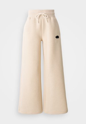 Pantaloni da jogging ampi beige realizzati in morbido tessuto, con vita elastica e cordoncino, e un piccolo logo nero sul lato.