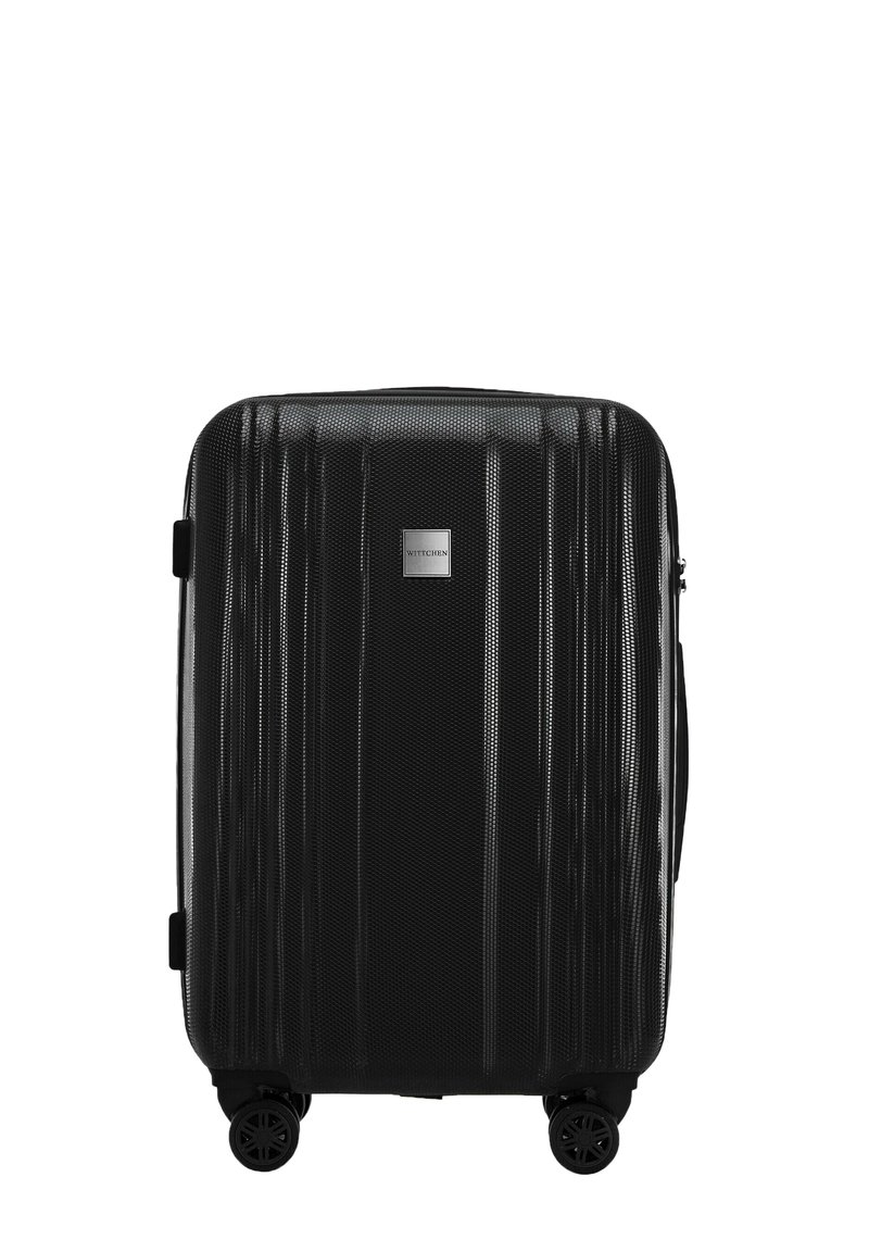 Valise rigide noire avec des rainures verticales, poignée robuste et quatre roues. Présente une plaque logo argentée à l'avant.