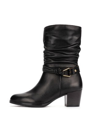 Black mid-calf leather boot with slouchy shaft, low block heel, and decorative strap with gold buckle around the ankle.