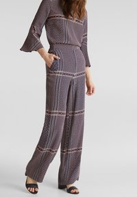 Mönstrad jumpsuit i marinblått, rött och krämfärgat. Har trumpetsärmar, vida ben och sidofickor. Materialet verkar lättviktigt och fladdrande.