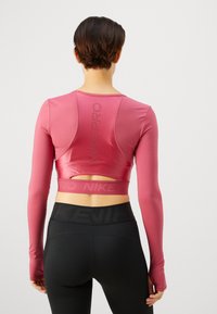 Garš piedurkņu, pieguļošs augšdaļa rozā krāsā ar izgriezumu aizmugurē. Ar "NIKE PRO" zīmolu atstarojošā tekstā. Apvienots ar melniem augstiem leggings.