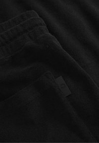 Black fleece fabric folded, showing fine texture and a subtle logo tag. The surface appears soft and plush, with no visible patterns.