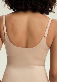 Nude, bezszwowy body z szerokimi ramiączkami i niskim dekoltem z tyłu. Posiada subtelny, teksturowany wzór na całej powierzchni materiału, co tworzy gładki wygląd.