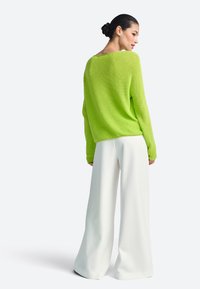 Limonkowo-zielony sweter dziergany o luźnym kroju oraz szerokie białe spodnie. Tkanina ma fakturowany wzór; sweter posiada szeroki dekolt i ściągacze na rękawach.