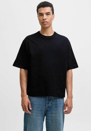 Tricou scurt negru din bumbac, cu un croi lejer și guler rotund, purtat cu blugi din denim de un bleu deschis.