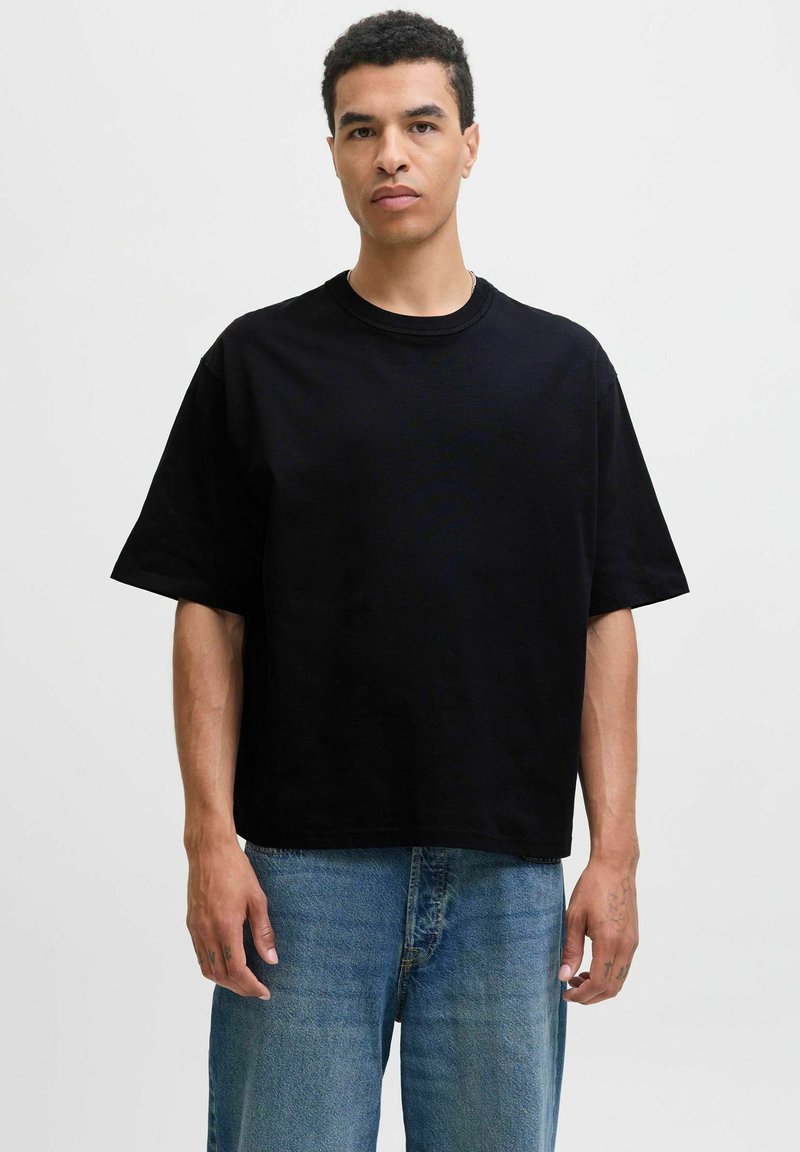 Sort T-shirt med kortærmer lavet af bomuld, med en afslappet pasform og rund halsudskæring, båret med lyseblå denimjeans.
