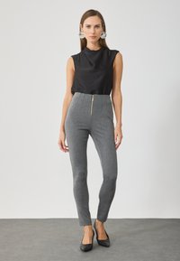 Gray high-waisted trousers with a smooth texture, featuring a front zip closure and vertical seam detailing. Paired with a black sleeveless top.