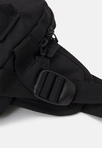 Czarna torba z materiału z mocnymi zamkami, teksturowaną powierzchnią, regulowanym paskiem oraz plastikową klamrą do bezpiecznego zamknięcia.