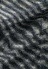 Texturált szövet, sötétkék és bézs színű tyúklábmintával, sima felülettel és enyhe fényességgel.