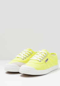 Zapatillas de lona amarillas limón con suelas de goma blancas, que cuentan con ojales metálicos, cordones blancos y una punta texturizada.