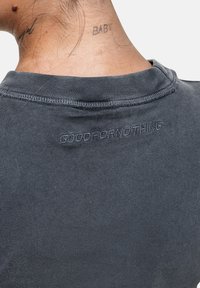 T-shirt in cotone grigio scuro con scollatura rotonda e il logo "GOOD FOR NOTHING" ricamato sulla schiena. Texture semplice.