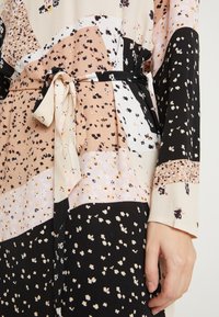 Vestido multicolorido con un patrón floral en tonos de rosa, negro y crema, con un cinturón de lazo y una textura de tela fluida.