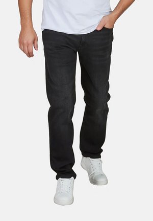 Zwarte denim jeans met een rechte snit, subtiele vervaging, gestikte details, gecombineerd met witte sneakers en een aansluitend wit T-shirt.