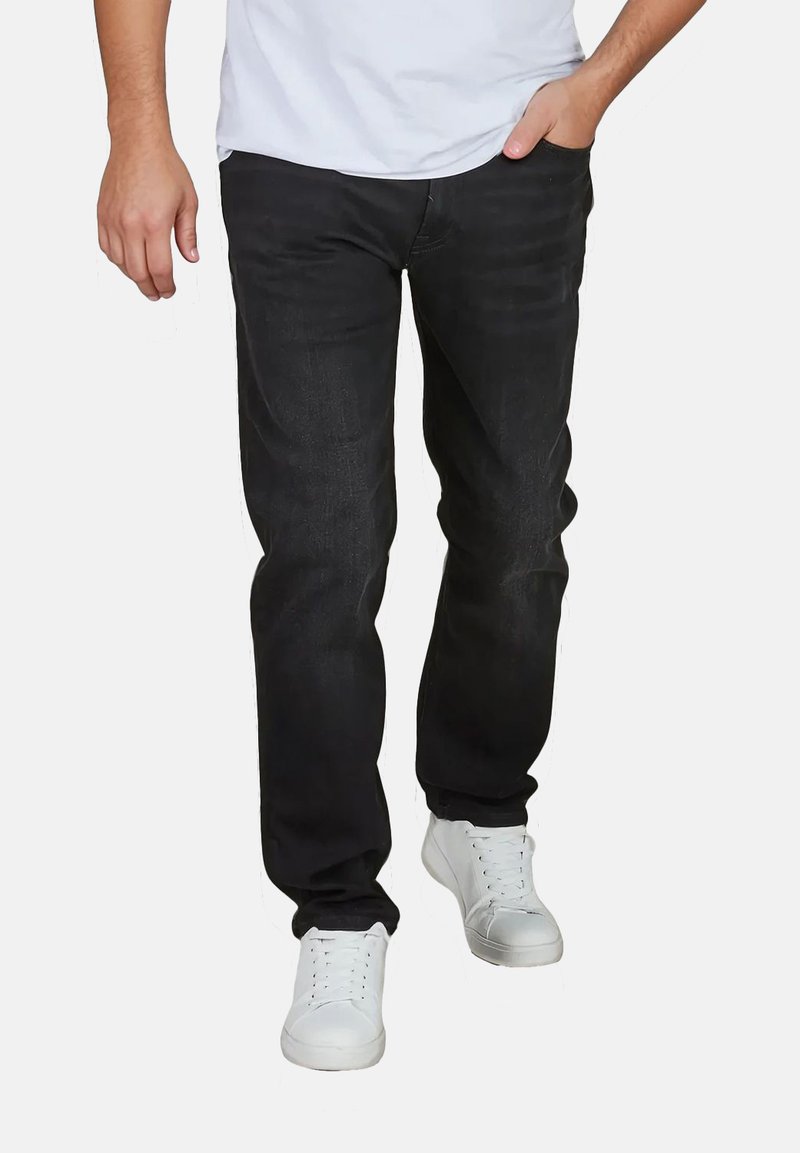 Zwarte denim jeans met een rechte snit, subtiele vervaging, gestikte details, gecombineerd met witte sneakers en een aansluitend wit T-shirt.