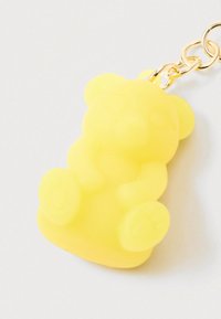 Sárga áttetsző, maci alakú kulcstartó arany színű lánccal, fehér háttéren.