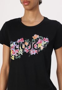 Black cotton t-shirt featuring a floral print with multicolored flowers and the "LIU JO" logo in the center, round neckline, short sleeves.