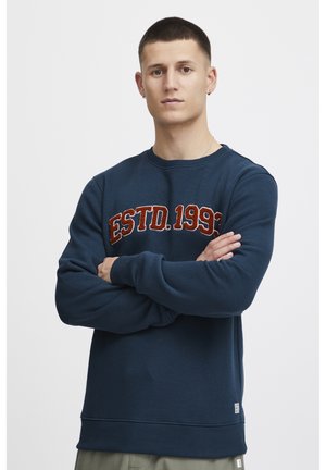Marineblauwe sweatshirt van een zachte, gestructureerde stof met ribbels aan de mouwen en onderkant. Voorzien van vet, rood geborduurd tekst met de tekst "ESTD. 1993."