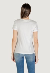 Camiseta blanca de algodón con mangas cortas enrolladas, cuello redondo, diseño ajustado y una textura suave. Combinada con unos vaqueros de mezclilla azul claro.