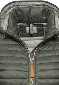 Reusable puffer jacket in dark green recycled material. Features a zip closure, textured quilted pattern, and an inner light gray lining.