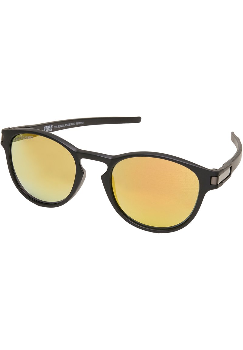 Lunettes de soleil avec une monture noire mate et des verres teintés jaunes. Design élégant et arrondi avec un logo discret sur la branche et des accents en métal.