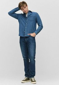 Sininen denim-paita nappilista ja rintatasku; yhdistetty sinisiin farkkuihin ja oliivinvihreisiin lenkkitossuihin, joissa on valkoiset nauhat.