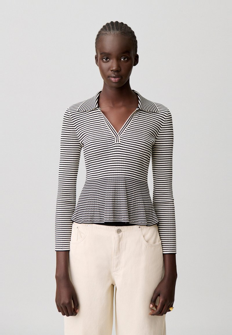 Top de manga larga con rayas blancas y negras, con cuello y escote en V; dobladillo acampanado, tejido suave, mangas ajustadas, combinado con pantalones de color claro.