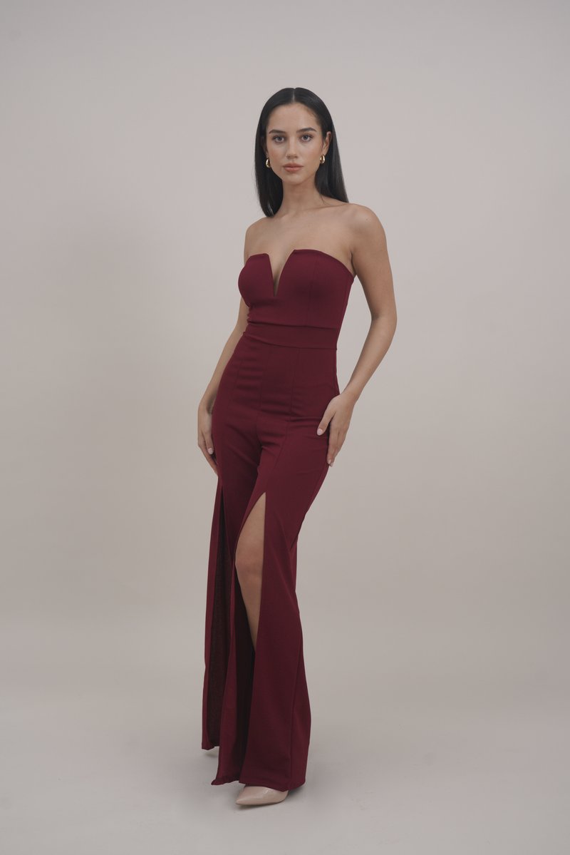Burgundy strapless jumpsuit with a deep V-neck, fitted bodice, and wide legs featuring thigh-high slits. Smooth, stretchy material.
