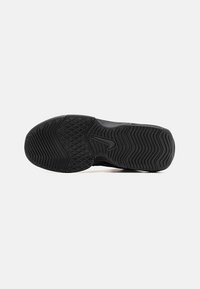 Semelle en caoutchouc noire d'une basket avec des motifs de bande de roulement variés et un logo swoosh central, vue de dessous sur un fond uni.
