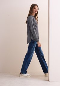 Grijs gestreepte blouse met lange mouwen en een ronde hals, gecombineerd met wijde donkerblauwe jeans en witte sneakers. Minimalistisch ontwerp en pasvorm.