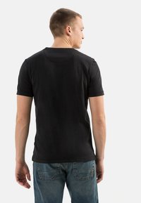 Schwarzes T-Shirt mit kurzen Ärmeln und rundem Halsausschnitt, von hinten gezeigt, kombiniert mit blauen Jeans.