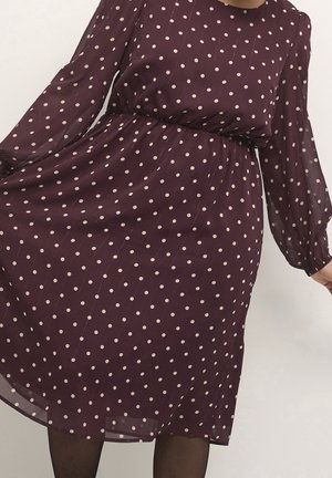 Donkerpaarse jurk met lange mouwen en lichtroze polkadots, getailleerde taille en doorschijnende stof aan de rok en mouwen.