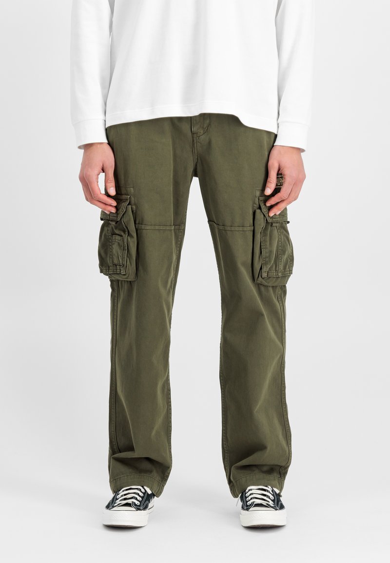 Olijfgroene cargobroek met twee grote zijzakken, een relaxed fit en omgeslagen boorden, gecombineerd met zwart-witte sneakers met een patroon.