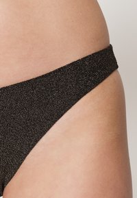 Parte de baixo de bikini preta com um acabamento texturizado e brilhante. A cintura fina assenta confortavelmente nos quadris, apresentando um design minimalista.
