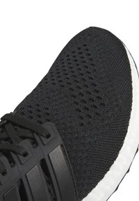 Μαύρο αθλητικό παπούτσι με υφασμάτινη επάνω επιφάνεια που αναπνέει, πλαστικές ιμάντες για στήριξη και λευκή μαλακή σόλα.