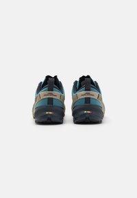 Chaussures de trail running avec un dessus en mesh bleu et gris foncé, dotées d'une semelle extérieure noire proéminente et de détails accentués multicolores.