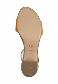 Beige sandal sula med rund form, slät gummibotten och en brun accent. Har en cirkulär metall-logotyp och strukturerade grepplinjer.
