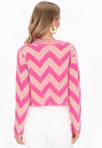 Ružová a žltá svetrová mikina s chevronovým vzorom, vyrobená z chlpatej látky, s dlhými rukávmi a okrúhlym výstrihom.
