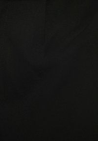 Detailní záběr hladké černé tkaniny s viditelným šitím a jemnými záhyby v jednolité tmavé textuře.